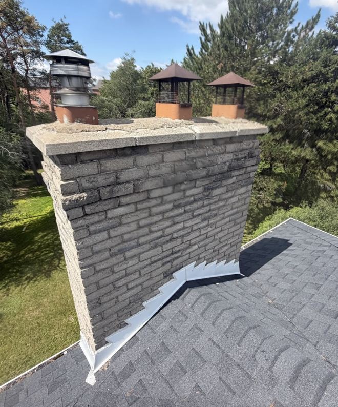 Rebuilt grey brick chimney with new caps and flashing on a shingle roof