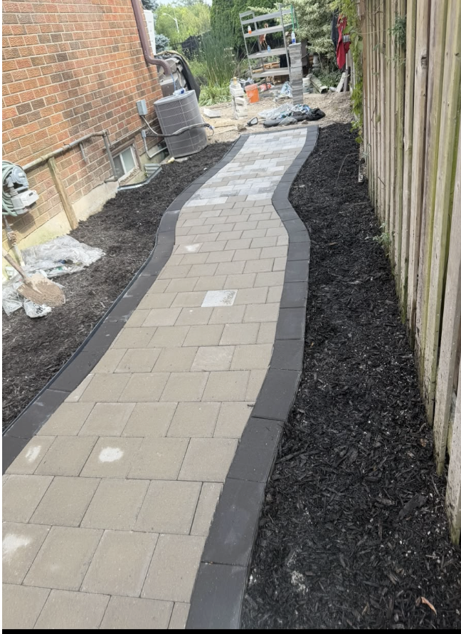 Newly laid curved concrete paver walkway beside a brick home