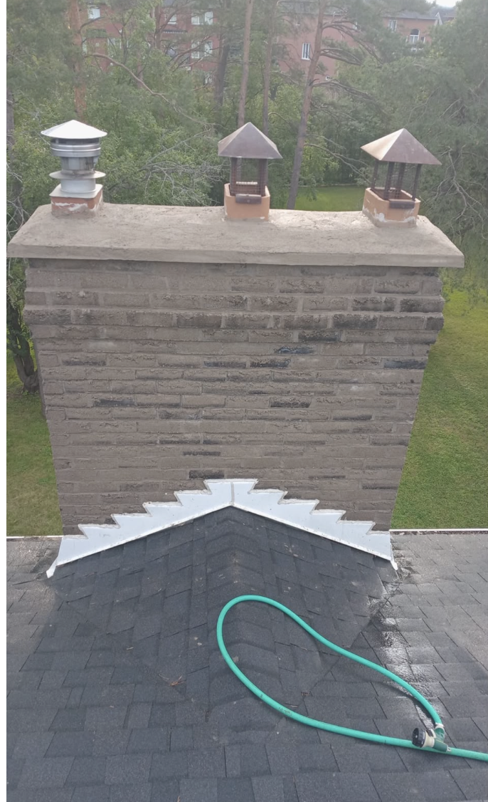 Front view of a grey brick chimney with three tops and roof flashing